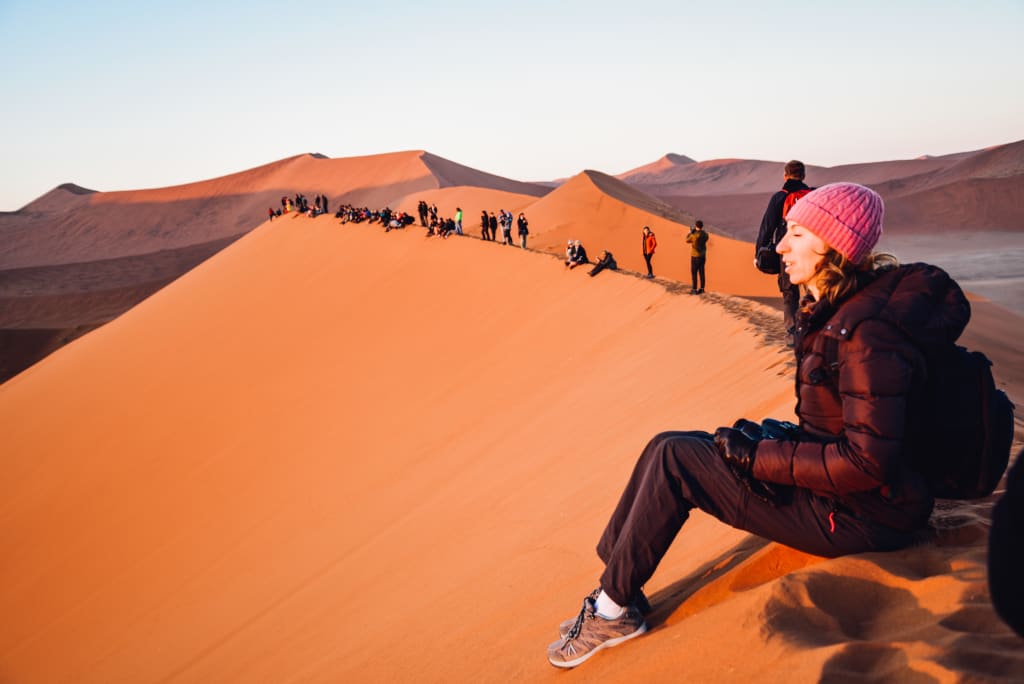 Fila di persone che si godono il tramonte da una duna nel deserto, Namibia